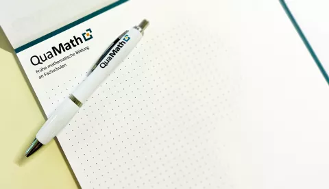 Ein Foto eines QuaMath-Schreibblocks auf dem ein Kugelschreiber liegt.